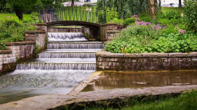 Brücke über Bachbett mit Wasserfall im Grünen